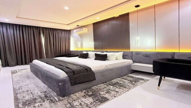 Een moderne slaapkamer met een groot bed, een nachtkastje, een sofa en een aan de muur bevestigde televisie.