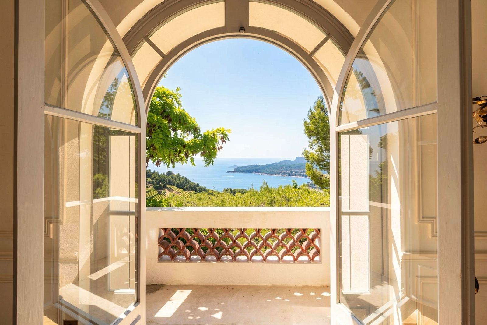 An arched window with a view of a coastal landscape, including vineyards and the sea.