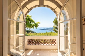 An arched window with a view of a coastal landscape, including vineyards and the sea.