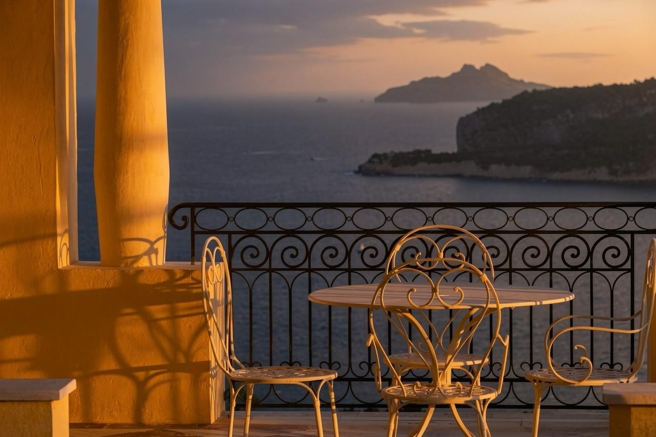 A balcony with a wrought iron railing, two chairs, and a small round table.