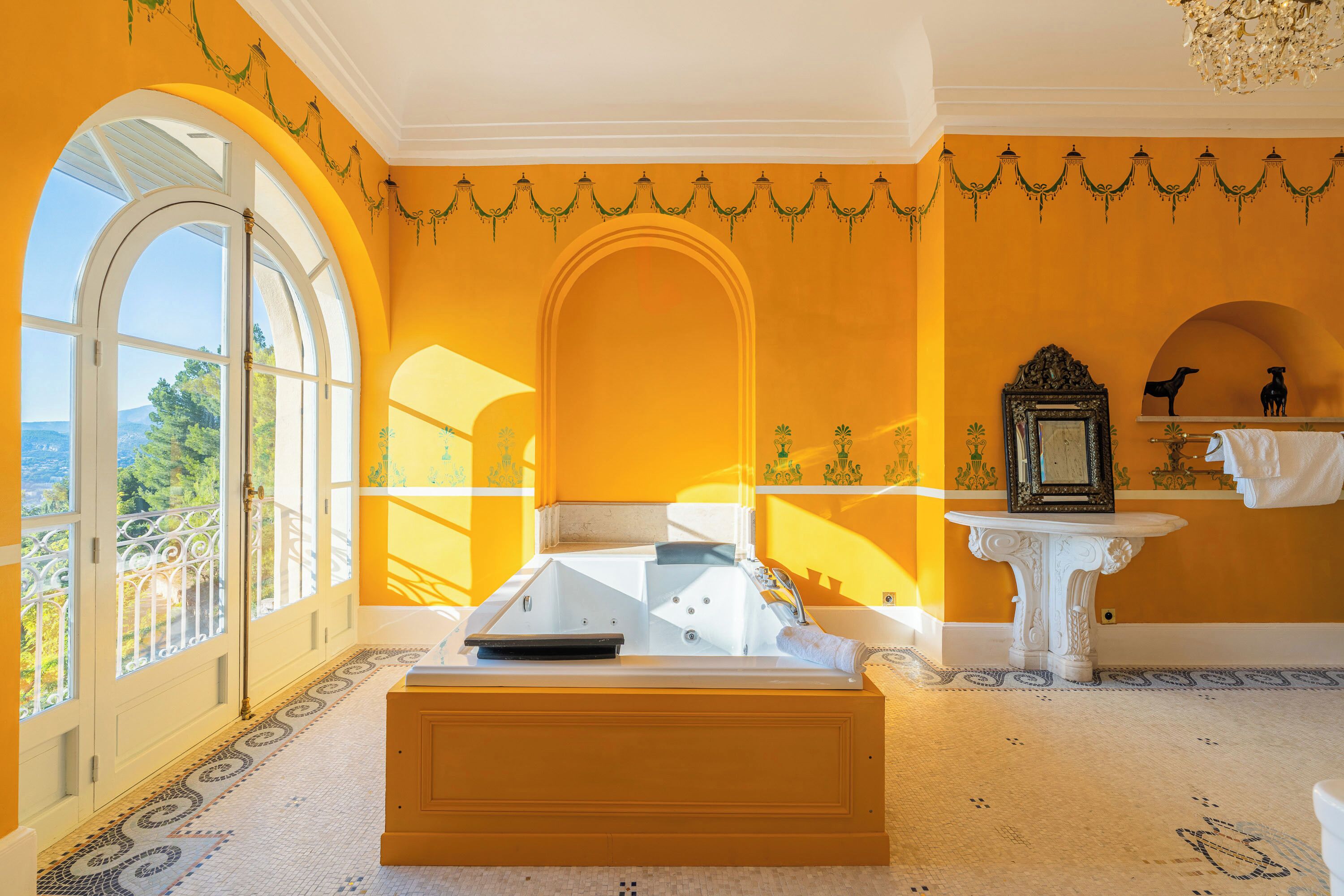 A room with a large arched window, a bathtub, and a small white pedestal with a mirror.