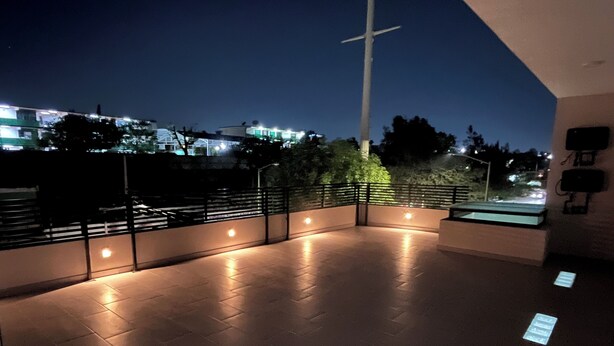 Eine Dachterrasse mit Geländer, einem Kreuz und Blick auf Gebäude im Hintergrund.