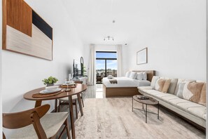 A modern hotel room with a dining area, a sofa, a coffee table, and a view of the city. - Free Housekeeping Visits During Your Stay - Stayshort - Relaxing Studio in Arjan That Sleeps 3 (Dubai)