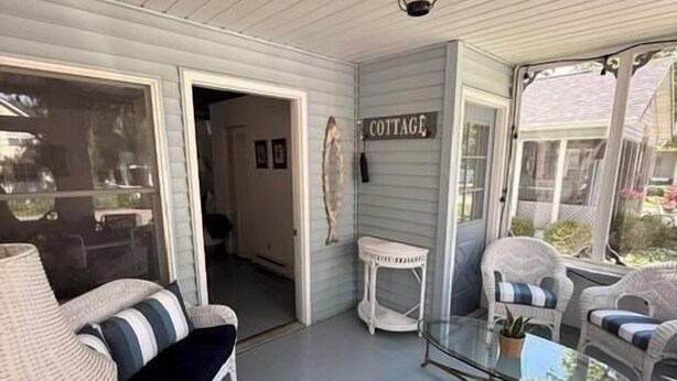 Eine überdachte Veranda mit Korbmöbeln, einem Glastisch und einem Schild mit der Aufschrift 'COTTAGE'.
