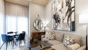 Una sala de estar moderna con una mesa de comedor redonda, sillas azules, un sofá beige y una obra de arte abstracta en la pared.