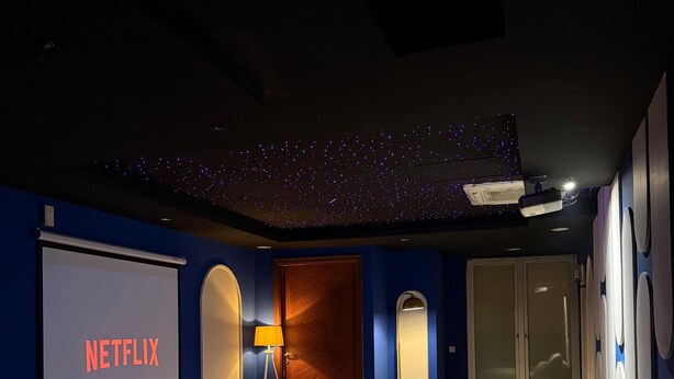 A dark room with a projector screen displaying 'NETFLIX,' a sofa, a lamp, and a ceiling with star-like lights. - luxury 1 bed apartment with indoor cinema,starlights & cityview in centre of DHA (Lahore)