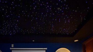 A room with a starry ceiling, a projection screen displaying 'NETFLIX,' a table with a stack of books and a horse figurine, and a floor lamp. - luxury 1 bed apartment with indoor cinema,starlights & cityview in centre of DHA (Lahore)