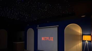 A room with a starry ceiling, a large screen displaying 'NETFLIX,' a small table with a sculpture, and a lamp.