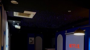 Ein Heimkinozimmer mit Projektor, einer Couch, einem Couchtisch und einem Bildschirm, der 'NETFLIX' anzeigt.