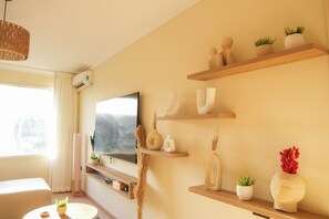 A modern living room with a flat-screen TV, wooden shelves with decorative items, and a window with curtains. - Pyramids View Suite (محافظة الجيزة)