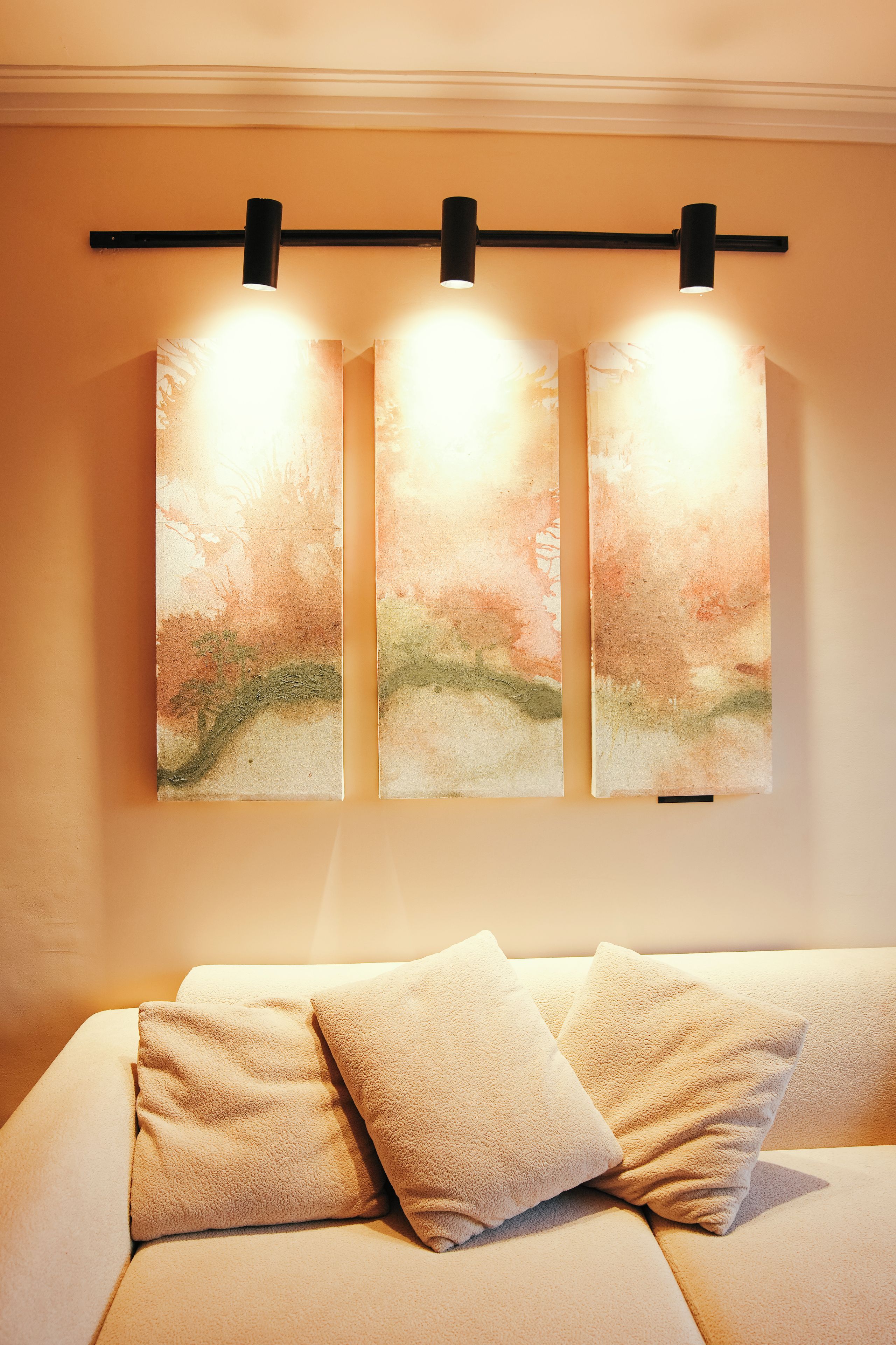 A wall with three illuminated panels and a sofa with cushions.