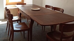 Un coin repas avec une longue table en bois, six chaises, une fenêtre laissant entrer la lumière naturelle et un ventilateur de plafond.