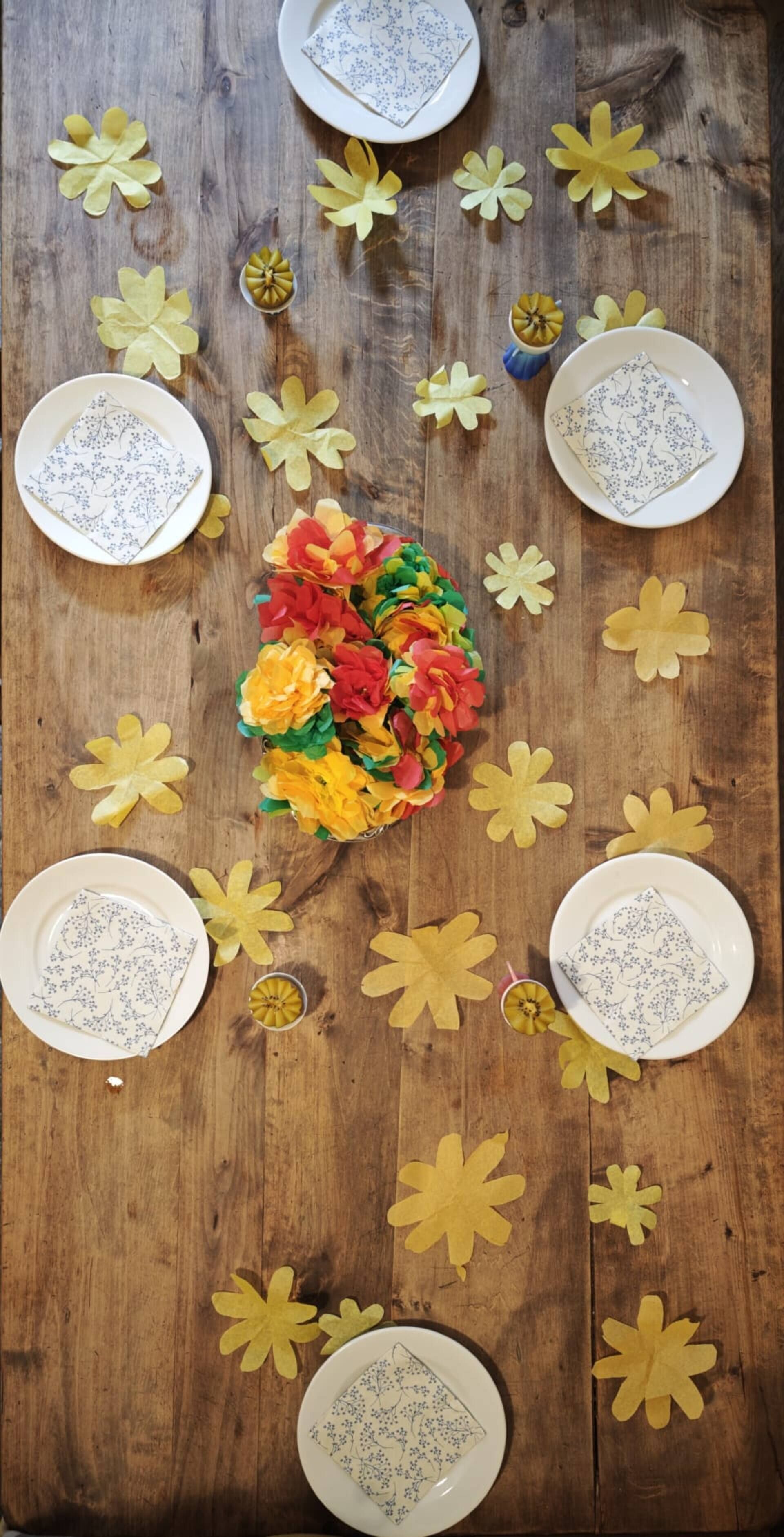 Ein Holztisch mit Papierblumen, Tellern und Servietten, die in einer kreisförmigen Anordnung platziert sind.
