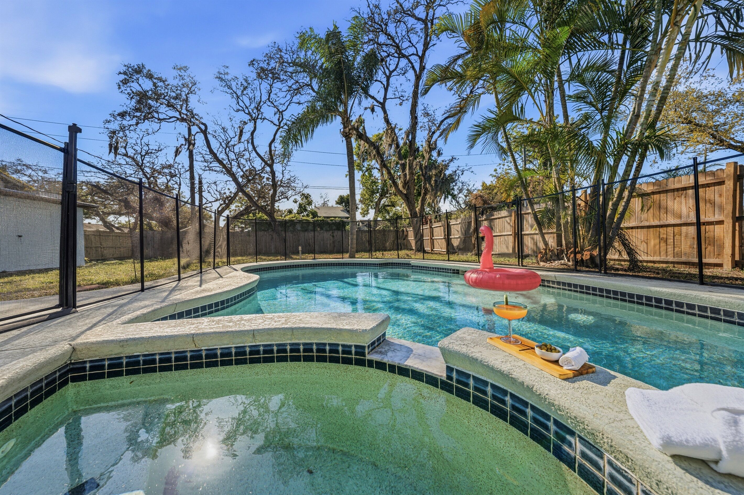 Una piscina con borde de azulejos, una cerca de madera y un flotador hinchable rojo.