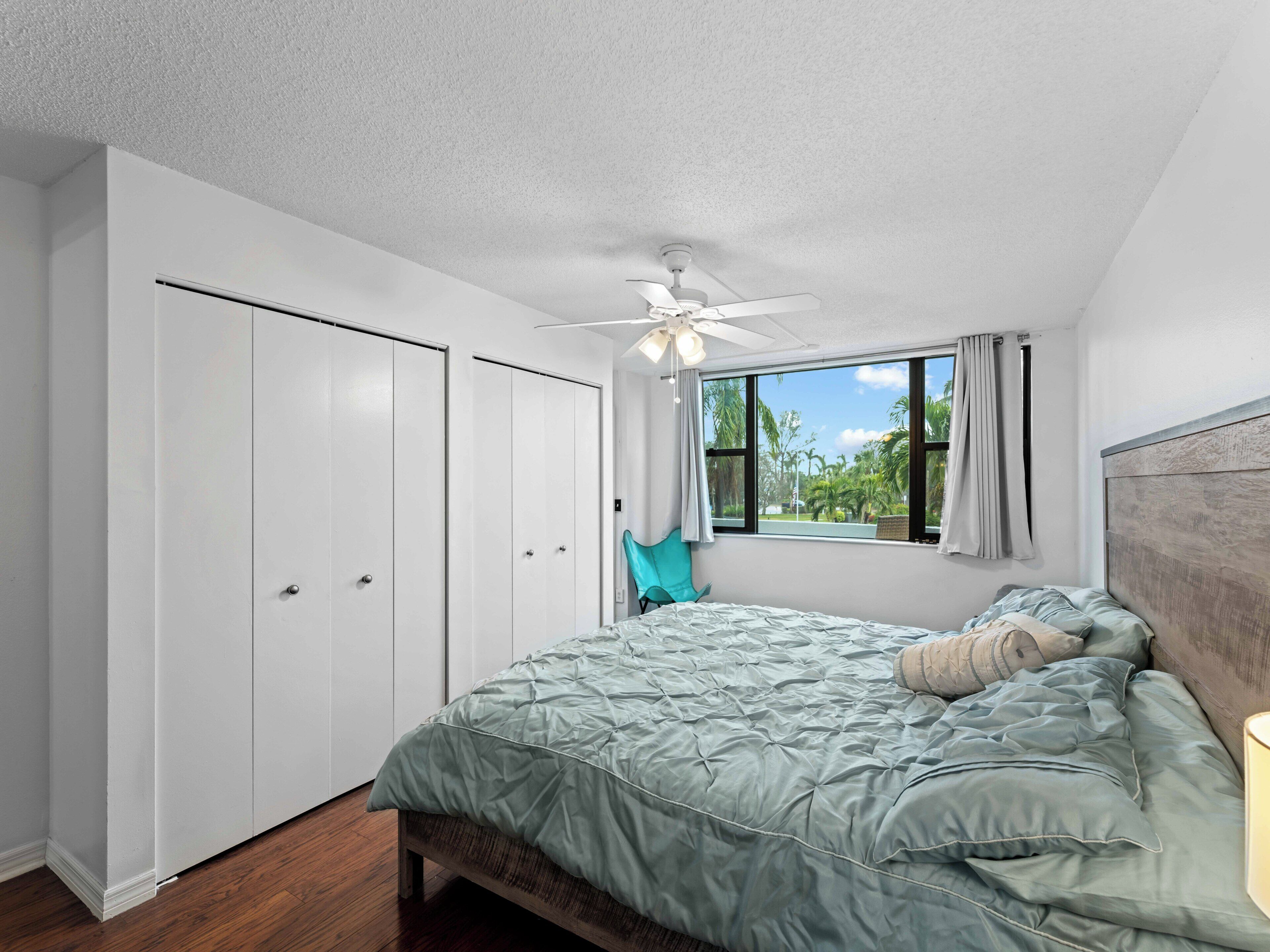 A bedroom with a bed, a ceiling fan, a window with curtains, and a wardrobe.