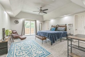 Een slaapkamer met een bed, een bureau, een stoel, een bankje, een plafondventilator en een groot raam.