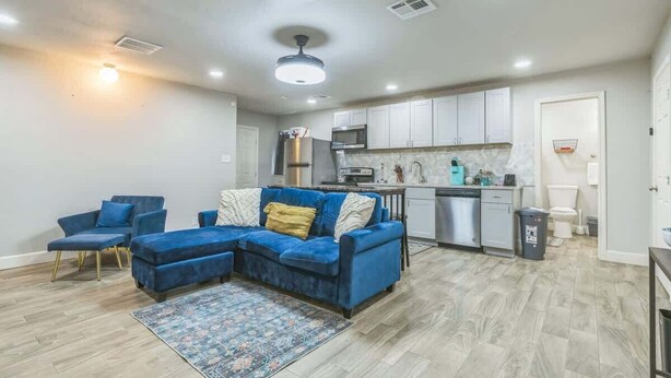 Uma sala de estar moderna com um sofá seccional, um pequeno espaço de jantar e uma cozinha compacta.