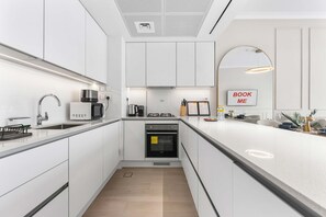 A modern kitchen with white cabinets, a built-in oven, a microwave, and a coffee maker. - Free Housekeeping Visits During Your Stay - Stayshort - Elegant 1 Bedroom in JVC Sleeps 4 With Balcony (Dubai)