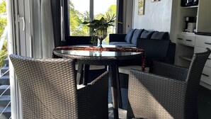 Ein modernes Wohnzimmer mit Glastisch, Korbstühlen, einer Couch und einer Küchenzeile.