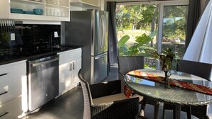 Eine moderne Küche mit Edelstahlgeräten, ein Essbereich mit Korbstühlen und Blick auf Grünflächen.