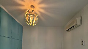 Ein Schlafzimmer mit einem Bett, einer Wand-Klimaanlage, einer Deckenleuchte und einem blauen Kleiderschrank.