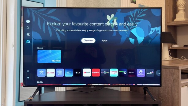 Ein Flachbildfernseher auf einem Standfuß, dessen Smart Hub verschiedene Streaming-Apps anzeigt.