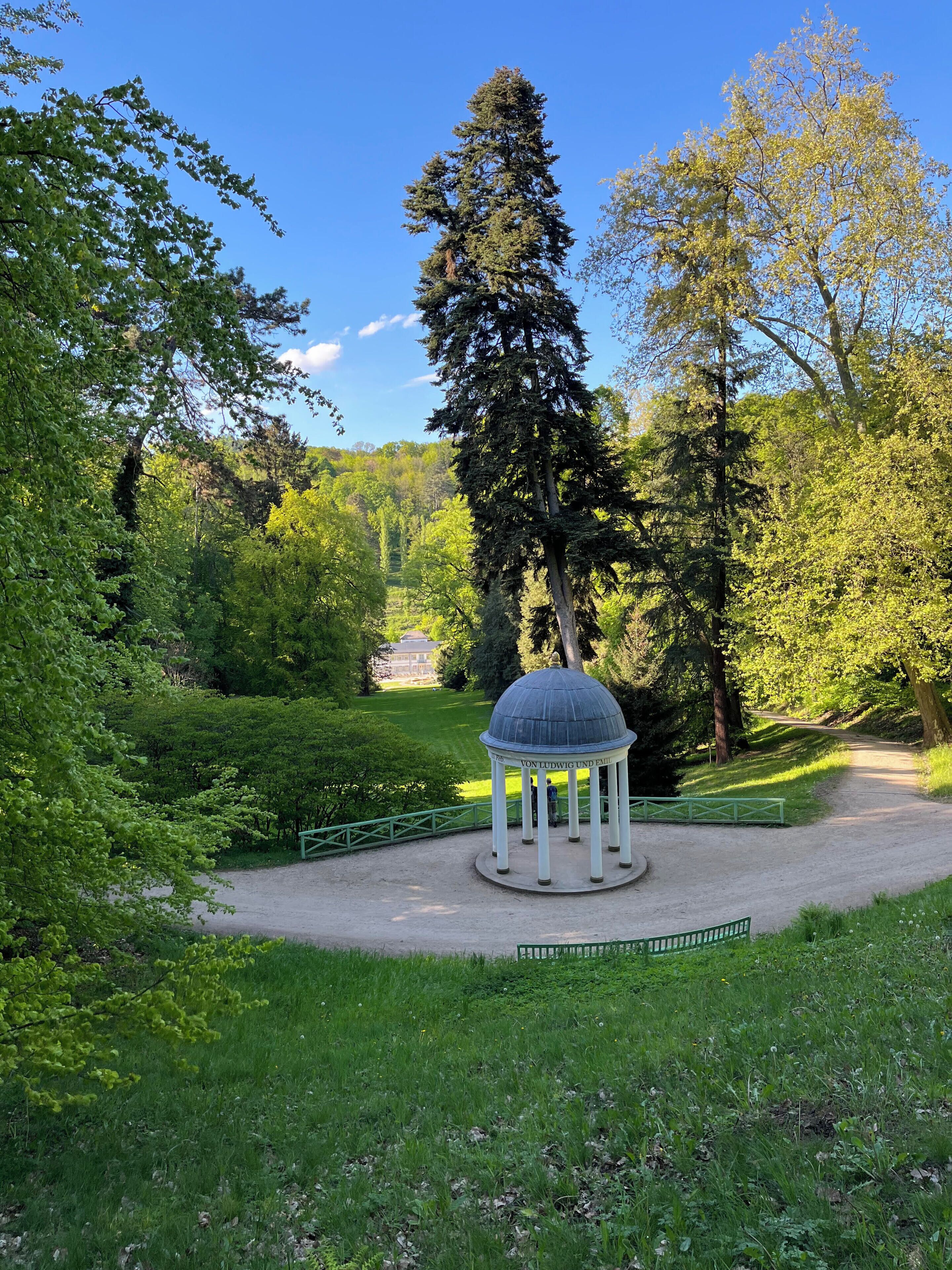 Ein Pavillon mit Kuppeldach, umgeben von üppiger Vegetation und Bäumen.