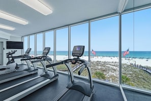 Ein Fitnessstudio mit Laufbändern und einem großen Fenster mit Blick auf einen Strand.