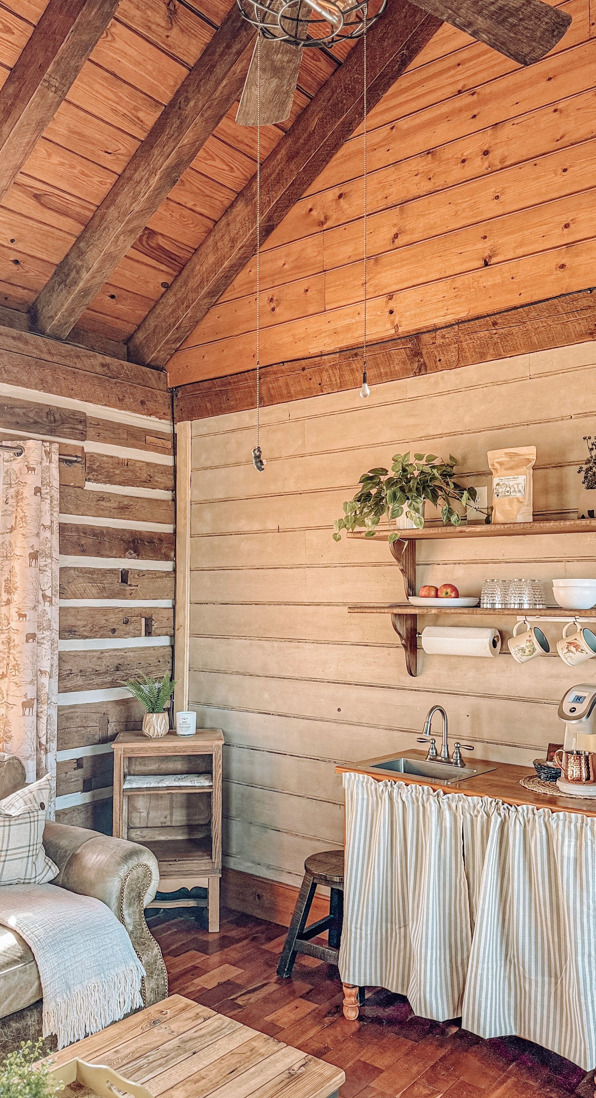 Un intérieur rustique en bois, avec un plafond en bois, une table à manger recouverte d’une nappe blanche, un banc en bois et un petit tabouret.