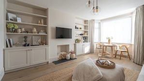 Una sala de estar moderna con un sofá, un televisor y una zona de comedor con una mesa y sillas.