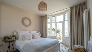 Un dormitorio con cama, mesita de noche con una planta, lámpara colgante y vistas amplias a través de grandes ventanales.