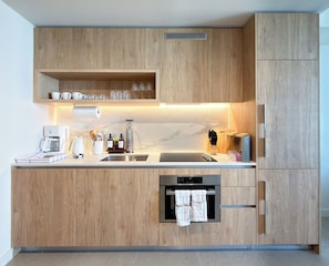 Een moderne keuken met houten kastjes, een inbouwoven, een koffiezetapparaat en een afwassysteem.