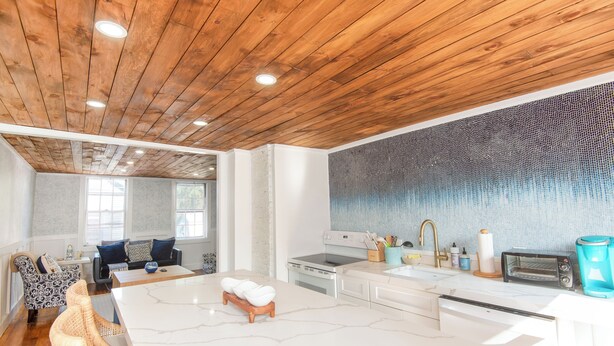 Una cucina moderna con un piano di lavoro in marmo, soffitto in legno e una parete di fondo decorata con un motivo blu.