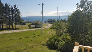 Ein Rasen mit einer Holzterrasse, freier Blick auf das Meer und einige Gebäude in der Ferne.