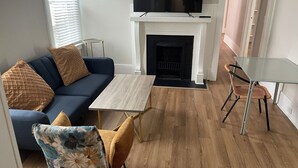 A living room with a sofa, a coffee table, a fireplace, and a TV mounted above it. - Stylish 3BR Apt in Savannah’s  Perfect for  Nurses, students  & Professionals! (Savannah)