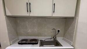 A compact kitchen with white cabinets, a stainless steel sink, and a built-in electric stove. - Self Checkin Studio - Olaya 203 (Riyadh)