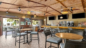 Zona de bar con diversas opciones de asientos, barra con una variedad de botellas y techo con diseño tejido y luces colgantes.
