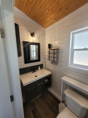 Un bagno moderno con un mobile lavabo bianco, pensili scuri, uno specchio, una lampada a sospensione, un portasciugamani e una finestra.