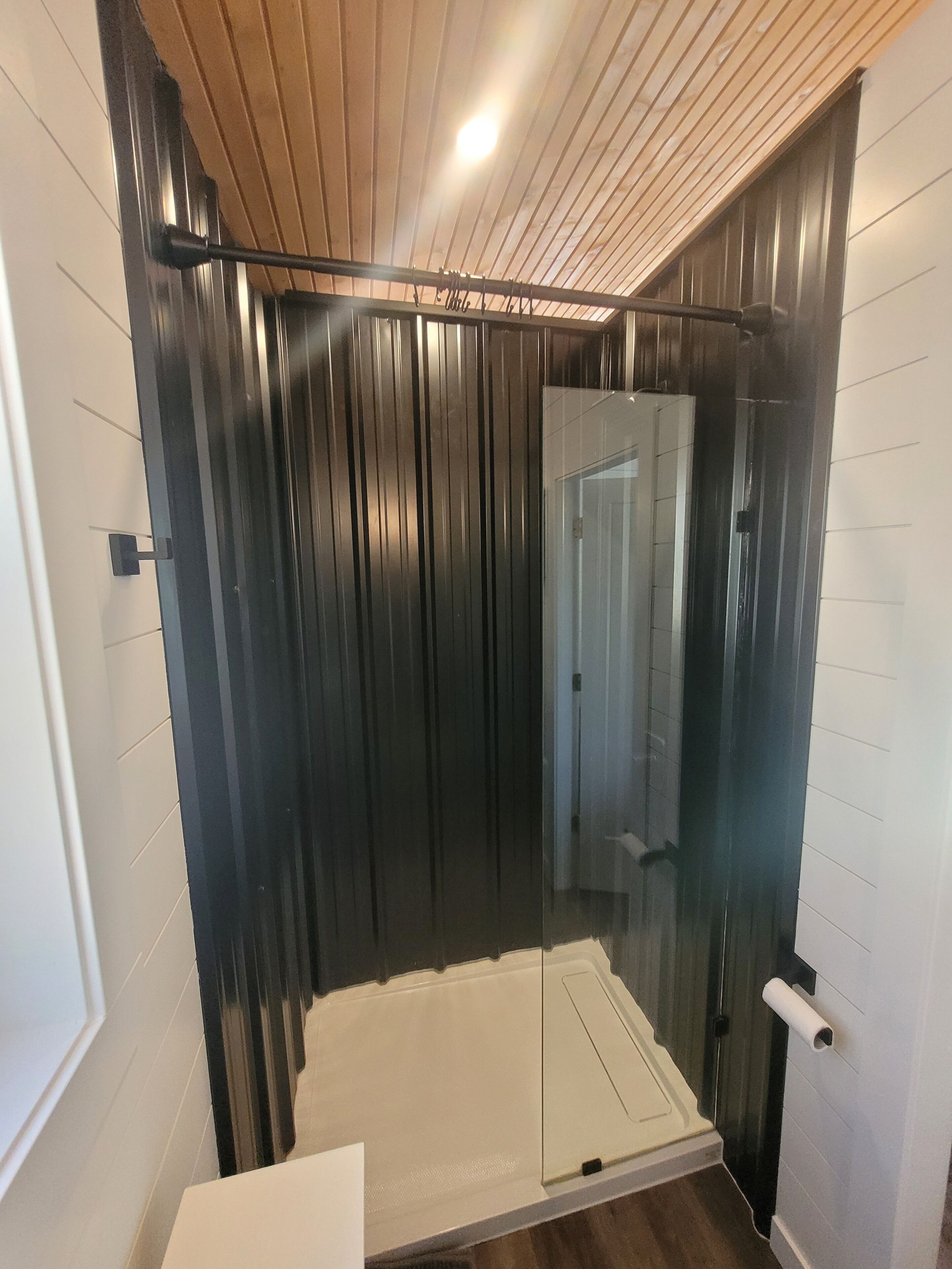 A shower with a glass door, a wooden ceiling, and a white wall.