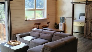 A modern living room with a sectional sofa, a dining table, and a large window with a view of the outdoors.