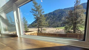 A room with a large window overlooking a mountainous landscape with trees and a wooden deck.