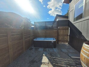 Una vasca idromassaggio in un giardino privato con recinzione in legno, un pontile di legno e vista su una montagna.