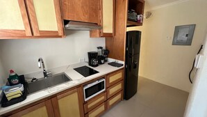 A kitchen with wooden cabinets, a black refrigerator, a coffee maker, and a microwave. - 1BR NEWLY REFURBISHED Apartment | Pool | Minutes to Oistins (Oistins)