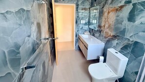 A bathroom with marble walls, a white sink, a toilet, and a glass shower enclosure. - 1BR NEWLY REFURBISHED Apartment | Pool | Minutes to Oistins (Oistins)
