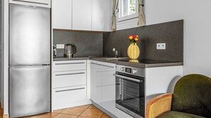 A compact kitchen with a refrigerator, oven, and a coffee maker. - Charming 1-bedroom apt 8 min walk to Monaco beach. Pool + Parking (Beausoleil)