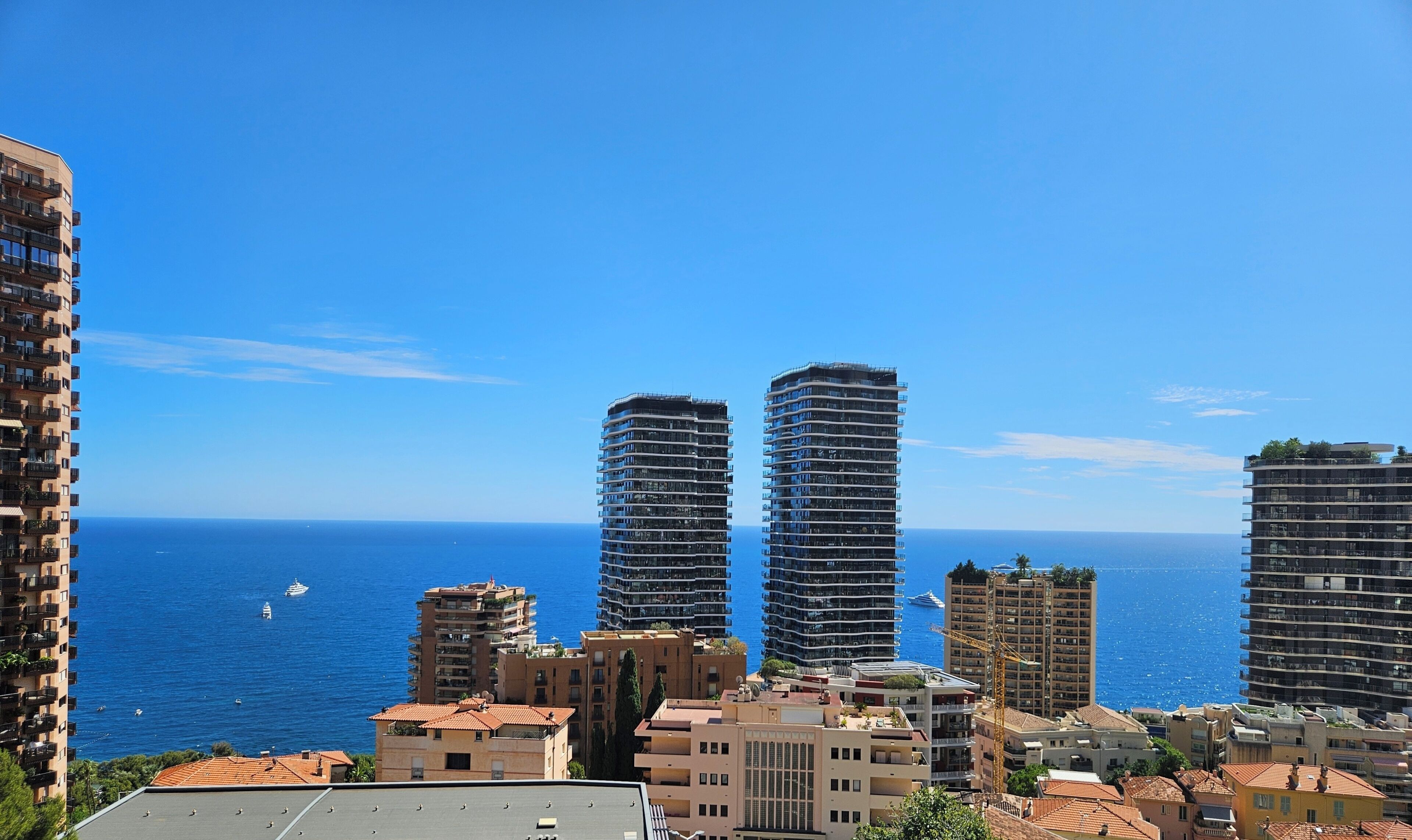 Un paysage urbain côtier avec de hauts immeubles, un ciel bleu dégagé et la mer en arrière-plan.