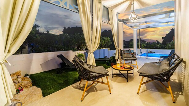 A rooftop terrace with two lounge chairs, a small table with a drink, and a pool in the background.