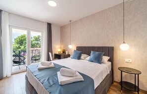 Ein Hotelzimmer mit einem großen Bett, einem kleinen Nachttisch, einem Sessel und Blick ins Freie.