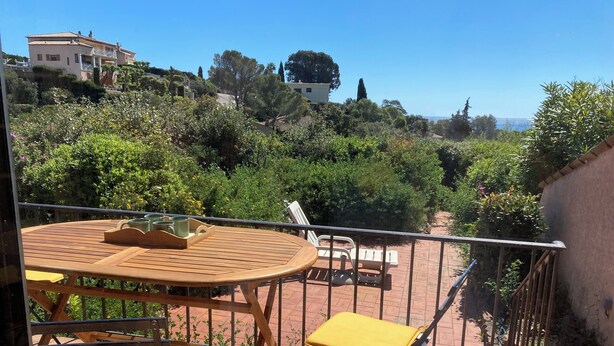 A wooden table and yellow chairs on a balcony with a view of trees and buildings. - Mazet garden level sea view close to calanques and beach (Saint-Raphaël)