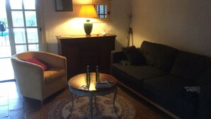 A living room with a sofa, armchair, coffee table, lamp, and a window. - Mazet garden level sea view close to calanques and beach (Saint-Raphaël)